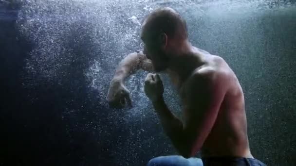 Boxeur d'athlète masculin sous l'eau, coups de poing d'entraînement et plongée sous la surface d'une piscine sombre — Video
