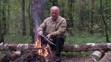 Yaşlı adam ormanda şenlik ateşi yakıyor, yürüyüşü durduruyor, doğada seyahat ediyor.