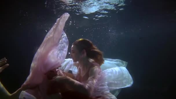 Passionate elegant lesbian couple in dresses hugging underwater, romance in the depths of the pool, slow motion — Stockvideo