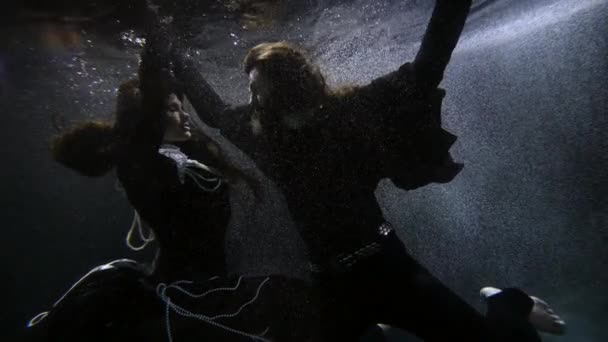 Красивая женщина в платье с жемчугом и драматический мужчина в черном танцуют под водой — стоковое видео