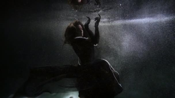 Mysterious woman in black gown is floating inside sea, river or pond, underwater enigmatic shot — Stockvideo
