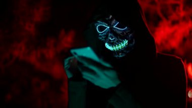 Kafatasının parlayan maskesi olan gizemli kişi akıllı telefon kullanıyor. Saldırgan isimsiz yorumlar.