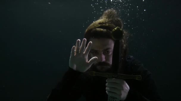 Knight or sorcerer with magic medieval sword is sinking in sea or lake, diving in depth and darkness — Stock Video