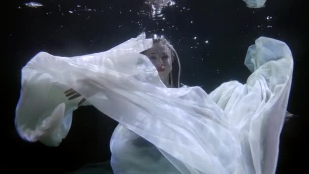 Сногсшибательная женщина плавает под водой, играя со своим шелковым белым платьем, замедленной съемки — стоковое видео