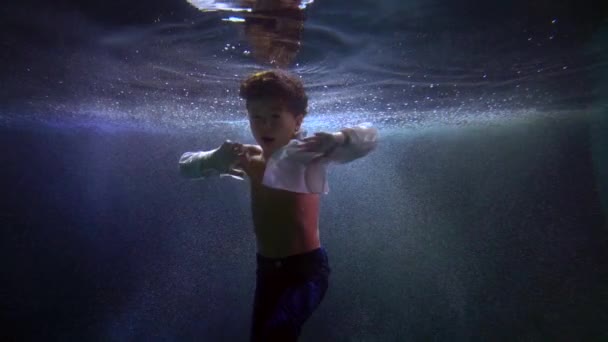 Lindo niño está girando dentro del agua de la piscina, niño flotando bajo el agua — Vídeos de Stock