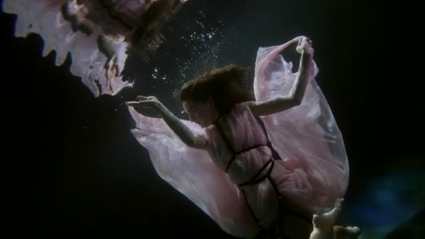 Femeie seducătoare tânără în rochie curgătoare plutește în adâncimea întunecată a mării, împușcat subacvatic — Videoclip de stoc