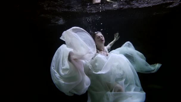 Verbazingwekkende mooie vrouw in witte jurk onderwater, drijvende vrouwelijke figuur in duisternis — Stockvideo