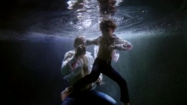 Yetişkin bir adam ve küçük bir çocuk suyun altında yüzüyor ve kavga ediyorlar, baba oğluna boks yapmayı öğretiyor.