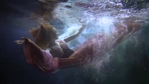 Graceful young ballerina is swimming alone in pool or sea, underwater romantic shot — Stockvideo