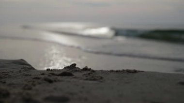 Kumsalda gün batımı, bulutlu bir akşamda beyaz kumsala doğru ilerleyen köpüklü dalgaların yavaş hareketidir.