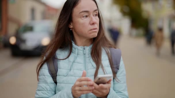 Portrait of an adult woman standing in an unfamiliar city and trying to find her way through an app on her phone — Stockvideo