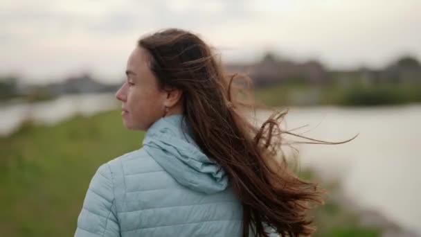 Close-up portrait of an adult woman, smiling, with long hair fluttering in the wind, walking quickly along the water in slow motion — Stock Video