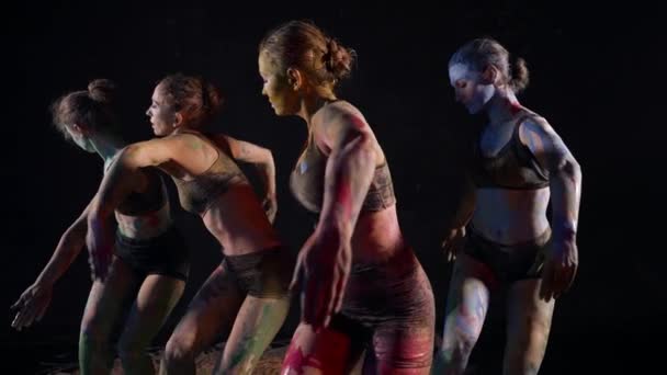 Синхронний танець чотирьох жінок-танцюристок, жінки танцюють у темряві, тіла вкриті фарбами — стокове відео