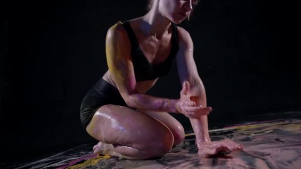 Contemporary art object, lady is drawing by her body and paints, sitting on floor in dark studio — Stock video