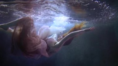 young beautiful woman is plunging in water of lake or pool, underwater slow motion shot