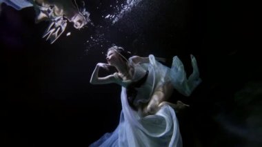 enchanted woman is floating underwater and touching her reflection in water reflection