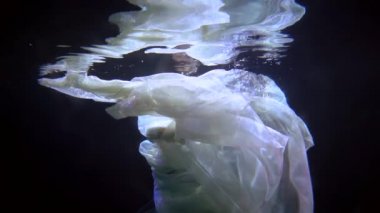 sensual underwater shot, woman is floating in dark depth, slow motion swimming