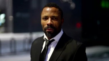 serious bearded black man is putting cap on head and looking at camera, outdoors portrait