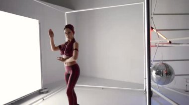 alluring woman is dancing in studio, seductive female figure against white glowing wall