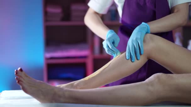 Beginning master of sugaring is removing hair from leg of female client in beauty salon — Stockvideo