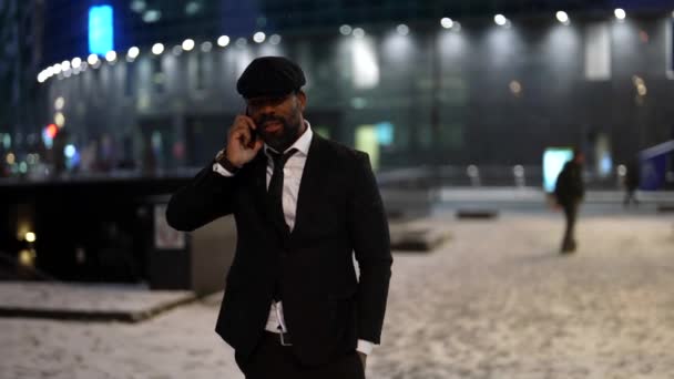 Carefree african businessman is talking by mobile phone on city street in winter evening — Video Stock