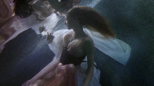Romantic and mysterious underwater shot with elegant young woman floating and playing with dress — Vídeo de Stock
