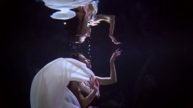 woman is floating inside depth and touching her reflection in water surface, underwater slow