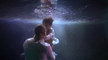 little boy is swimming underwater, embracing his dad, subaquatic shot of man and his son in pool