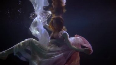 romantic nymph of lake or sea is swimming alone in dark depth, slow motion underwater shot