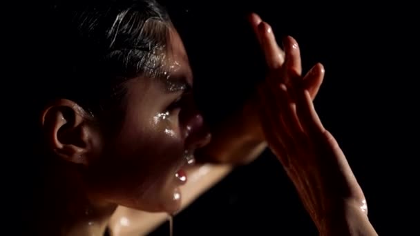 Emotional woman in shower or rain, playing with light sensually, water is flowing over face — Stockvideo