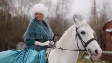 smiling lady in old-fashioned gown is riding horse in winter, vintage and retro style