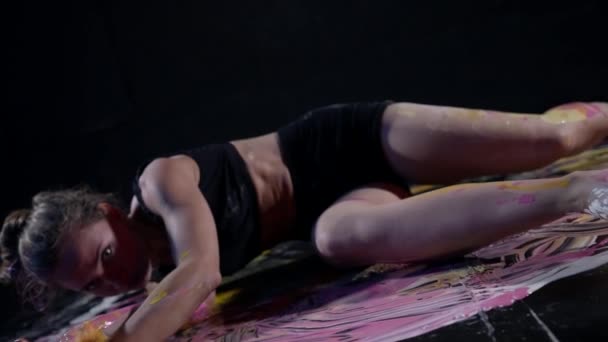 Сумасшедшая и расстроенная юная леди лежит на полу в художественной студии и размазывает краски — стоковое видео