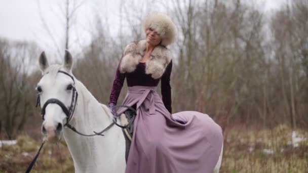 Pretty lady in old-fashioned gown is sitting on horseback in forest, horse riding in nature in winter — Video