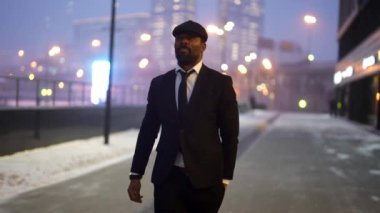 successful stylish black man is strolling on city street in winter evening, night city life