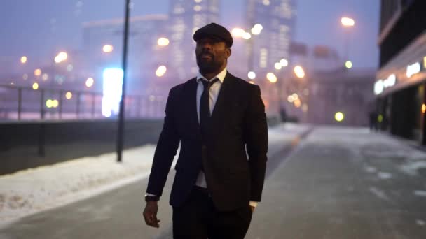 Successful stylish black man is strolling on city street in winter evening, night city life — Stock Video