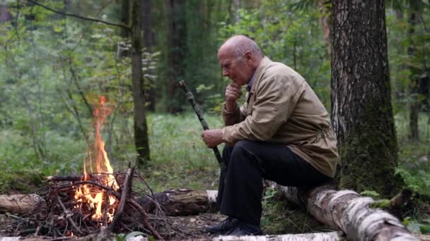 An old hunter is resting, cold weather and a fire warms an elderly man — Stock video