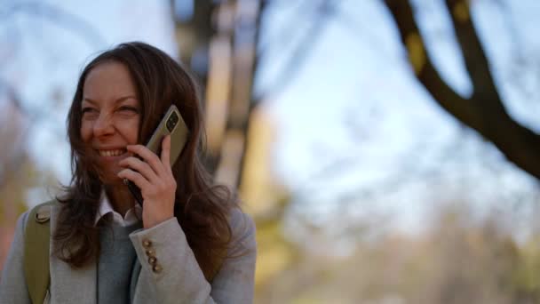 Laughing woman is calling by mobile phone, portrait in park during walk in sunny weather — Stok video
