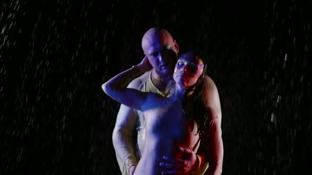 Mysterious sensual lovers in rain in darkness, man is hugging woman with face mask — Stockvideo