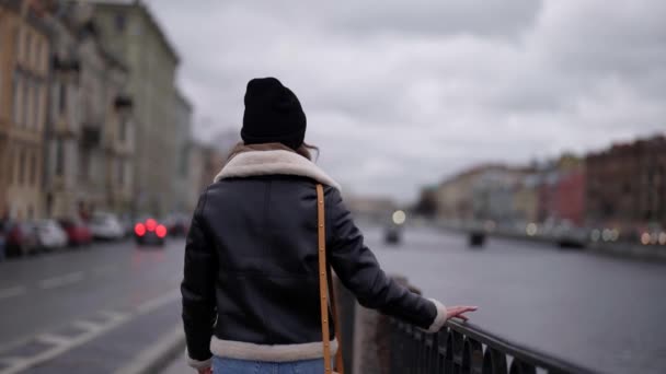 Ung kvinna i svart jacka går ensam på stadsvall i höst eller vinter dag — Stockvideo