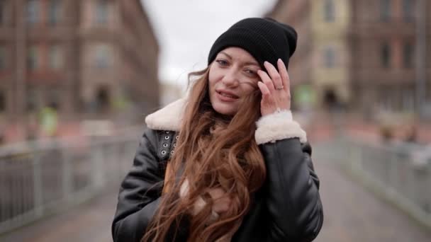 Porträt einer hübschen jungen Frau in der Stadt an einem Herbsttag, Passantin trägt Hut und Jacke — Stockvideo