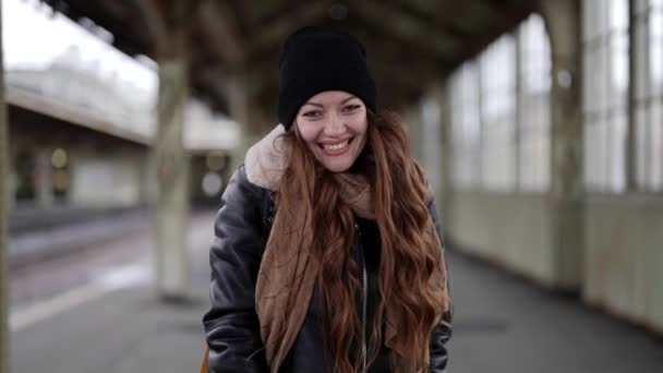 Glückliche blauäugige Frau lächelt in die Kamera, wenn sie im Herbst oder Winter im Bahnhof spazieren geht — Stockvideo
