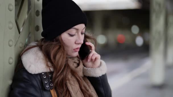 Overstuur jonge vrouw is praten door mobiele telefoon in het station in de winter, close-up portret — Stockvideo
