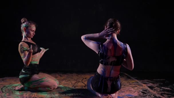 Dwie seksowne kobiety wykonują ruchy tańca współczesnego, siedząc na podłodze z barwnikami — Wideo stockowe