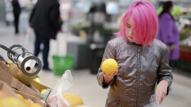 Barn oberoende att göra inköp för att hjälpa föräldrar. En flicka med rosa hår i snabbköpet väljer frukt — Stockvideo