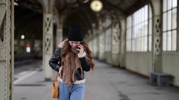 Ung kvinna väntar tåg på stationen och ringer via mobiltelefon, promenader på plattform — Stockvideo