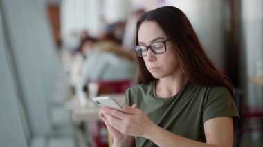 Yetişkin gülümseyen kadın akıllı telefonuyla mesaj gönderiyor, kafede tek başına oturuyor.