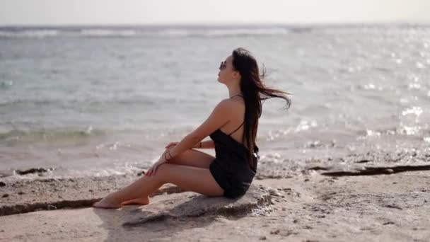 セクシーな女性は一人でビーチに座って夏の日に海の景色を賞賛している — ストック動画