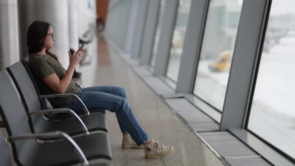 Pasajero femenino está esperando el embarque en el aeropuerto, navegar por Internet por teléfono móvil — Vídeo de stock