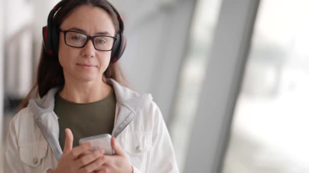 Desfrutar de música on-line por smartphone, mulher morena está ouvindo música por fones de ouvido sem fio — Vídeo de Stock