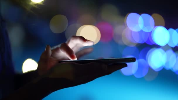 Modernes Smartphone in den Händen einer Nutzerin, Nahaufnahme vor verschwommenem Lichthintergrund — Stockvideo
